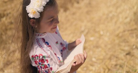 Wall Mural - Girl in bulgarian embroidery ethnic folklore costume reading book on a harvesting wheat field, Bulgaria