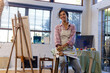 © Wavebreak Media - Happy biracial woman wearing apron holding brushes in home studio