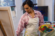 © Wavebreak Media - Biracial woman wearing apron painting on easel using colour palette in home studio