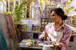 © Wavebreak Media - Biracial woman wearing apron painting on easel using brush and colour palette in garden