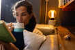 © Wavebreak Media - Biracial woman sitting on sofa, holding mug and reading book