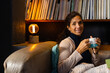 © Wavebreak Media - Portrait of happy biracial woman sitting on sofa holding mug and smiling in living room, copy space