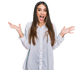 Wall Mural - Young beautiful woman wearing casual white shirt celebrating victory with happy smile and winner expression with raised hands