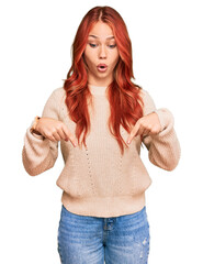 Poster - Young redhead woman wearing casual winter sweater pointing down with fingers showing advertisement, surprised face and open mouth