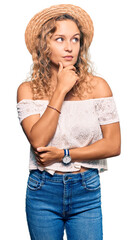 Wall Mural - Beautiful caucasian woman wearing summer hat with hand on chin thinking about question, pensive expression. smiling with thoughtful face. doubt concept.