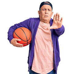 Poster - Senior handsome grey-haired man holding basketball ball with open hand doing stop sign with serious and confident expression, defense gesture