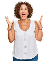 Wall Mural - Beautiful middle age mature woman wearing casual white shirt celebrating crazy and amazed for success with arms raised and open eyes screaming excited. winner concept