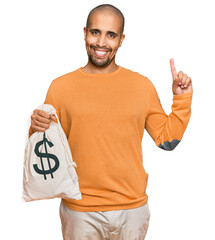 Poster - Hispanic adult man holding dollars bag surprised with an idea or question pointing finger with happy face, number one