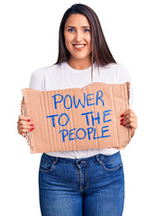 Wall Mural - Young beautiful woman holding power to the people cardboard banner looking positive and happy standing and smiling with a confident smile showing teeth