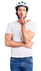 Canvas Print - Young handsome man wearing bike helmet looking at the camera blowing a kiss with hand on air being lovely and sexy. love expression.