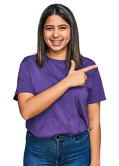 Sticker - Young hispanic girl wearing casual purple t shirt cheerful with a smile of face pointing with hand and finger up to the side with happy and natural expression on face