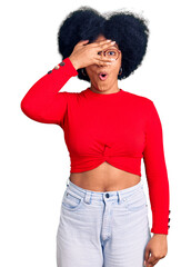 Sticker - Young african american girl wearing casual clothes and glasses peeking in shock covering face and eyes with hand, looking through fingers with embarrassed expression.