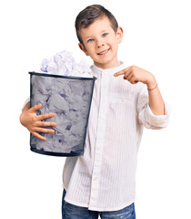 Sticker - Cute blond kid holding paper bin full of crumpled papers smiling happy pointing with hand and finger