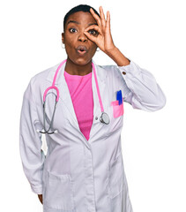 Poster - Young african american woman wearing doctor uniform and stethoscope doing ok gesture shocked with surprised face, eye looking through fingers. unbelieving expression.