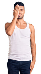 Wall Mural - Young hispanic man wearing casual clothes covering one eye with hand, confident smile on face and surprise emotion.