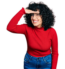 Poster - Young middle east girl wearing casual clothes and glasses very happy and smiling looking far away with hand over head. searching concept.