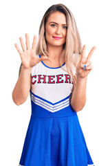 Canvas Print - Young beautiful blonde woman wearing cheerleader uniform showing and pointing up with fingers number seven while smiling confident and happy.