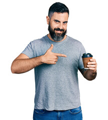 Wall Mural - Hispanic man with beard drinking a take away cup of coffee smiling happy pointing with hand and finger