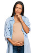 © Krakenimages.com - Beautiful hispanic woman expecting a baby showing pregnant belly serious face thinking about question with hand on chin, thoughtful about confusing idea