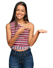 Sticker - Beautiful hispanic woman wearing casual clothes amazed and smiling to the camera while presenting with hand and pointing with finger.