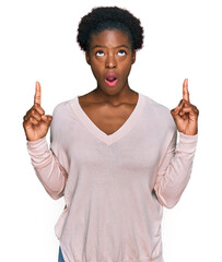 Canvas Print - Young african american girl wearing casual clothes amazed and surprised looking up and pointing with fingers and raised arms.