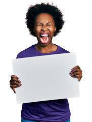 Wall Mural - African american woman with afro hair holding blank empty banner angry and mad screaming frustrated and furious, shouting with anger looking up.