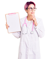 Canvas Print - Young beautiful woman with pink hair wearing doctor stethoscope holding clipboard with medical report serious face thinking about question with hand on chin, thoughtful about confusing idea