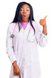 © Krakenimages.com - Young african american woman wearing doctor stethoscope surprised pointing with hand finger to the side, open mouth amazed expression.