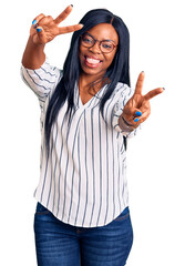 Poster - Young african american woman wearing casual clothes and glasses smiling with tongue out showing fingers of both hands doing victory sign. number two.