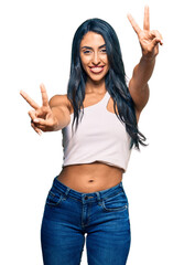 Wall Mural - Beautiful hispanic woman wearing casual clothes smiling with tongue out showing fingers of both hands doing victory sign. number two.