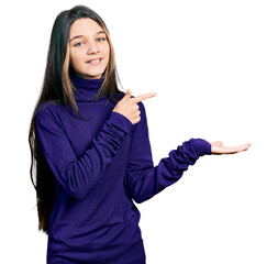 Canvas Print - Young brunette girl with long hair wearing turtleneck sweater amazed and smiling to the camera while presenting with hand and pointing with finger.