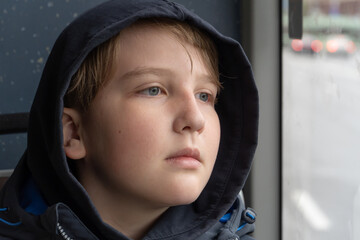 A ten-year-old boy in a hood near the window rides on a bus. Close-up