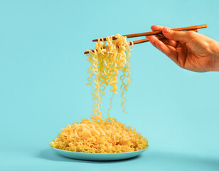 Egg noodles on blue plate and female hands with chopsticks on blue background