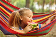 © Inna Vlasova - Cute little girl resting in a colored hammock in the forest and eating fresh watermelon