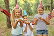 © Inna Vlasova - Children holding birthday cakes with burning candles. Kids party decoration and food. Boy and girls celebrating birthday in the garden with hammock. Kids with sweets.