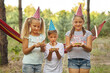 © Inna Vlasova - Children holding birthday cakes with burning candles. Kids party decoration and food. Boy and girls celebrating birthday in the garden with hammock. Kids with sweets.