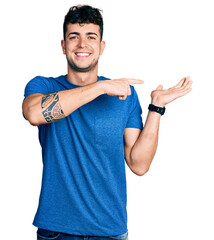 Wall Mural - Young hispanic man wearing casual t shirt amazed and smiling to the camera while presenting with hand and pointing with finger.