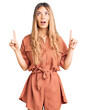 © Krakenimages.com - Beautiful caucasian woman with blonde hair wearing summer jumpsuit amazed and surprised looking up and pointing with fingers and raised arms.