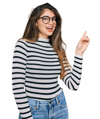 Wall Mural - Young beautiful teen girl wearing casual clothes and glasses with a big smile on face, pointing with hand and finger to the side looking at the camera.