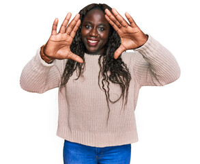 Sticker - Young african woman wearing wool winter sweater doing frame using hands palms and fingers, camera perspective