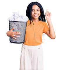 Sticker - Cute african american girl holding paper bin full of crumpled papers surprised with an idea or question pointing finger with happy face, number one