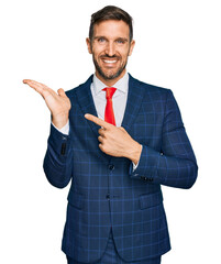 Canvas Print - Handsome man with beard wearing business suit and tie amazed and smiling to the camera while presenting with hand and pointing with finger.