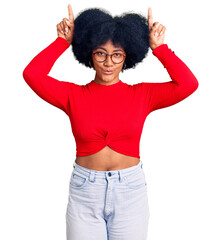 Sticker - Young african american girl wearing casual clothes and glasses doing funny gesture with finger over head as bull horns