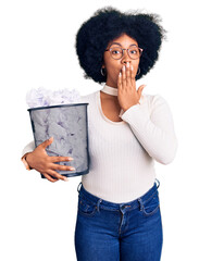 Poster - Young african american girl holding paper bin full of crumpled papers covering mouth with hand, shocked and afraid for mistake. surprised expression