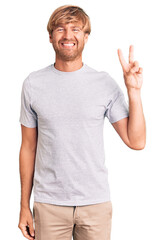 Canvas Print - Handsome caucasian man with beard wearing casual tshirt smiling with happy face winking at the camera doing victory sign. number two.