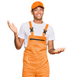 © Krakenimages.com - Young handsome african american man wearing handyman uniform clueless and confused expression with arms and hands raised. doubt concept.