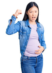 Canvas Print - Young beautiful chinese woman pregnant expecting baby angry and mad raising fist frustrated and furious while shouting with anger. rage and aggressive concept.