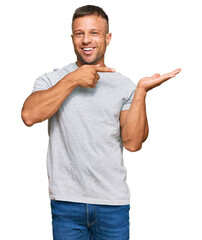 Canvas Print - Handsome muscle man wearing casual grey tshirt amazed and smiling to the camera while presenting with hand and pointing with finger.