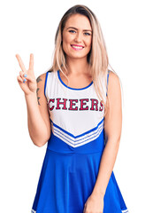 Wall Mural - Young beautiful blonde woman wearing cheerleader uniform smiling looking to the camera showing fingers doing victory sign. number two.