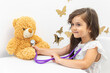 Little child girl plays with plush toy at doctor appointment. Child listens to soft toy with stethoscope. Doctors concept for children, copy space for text.
